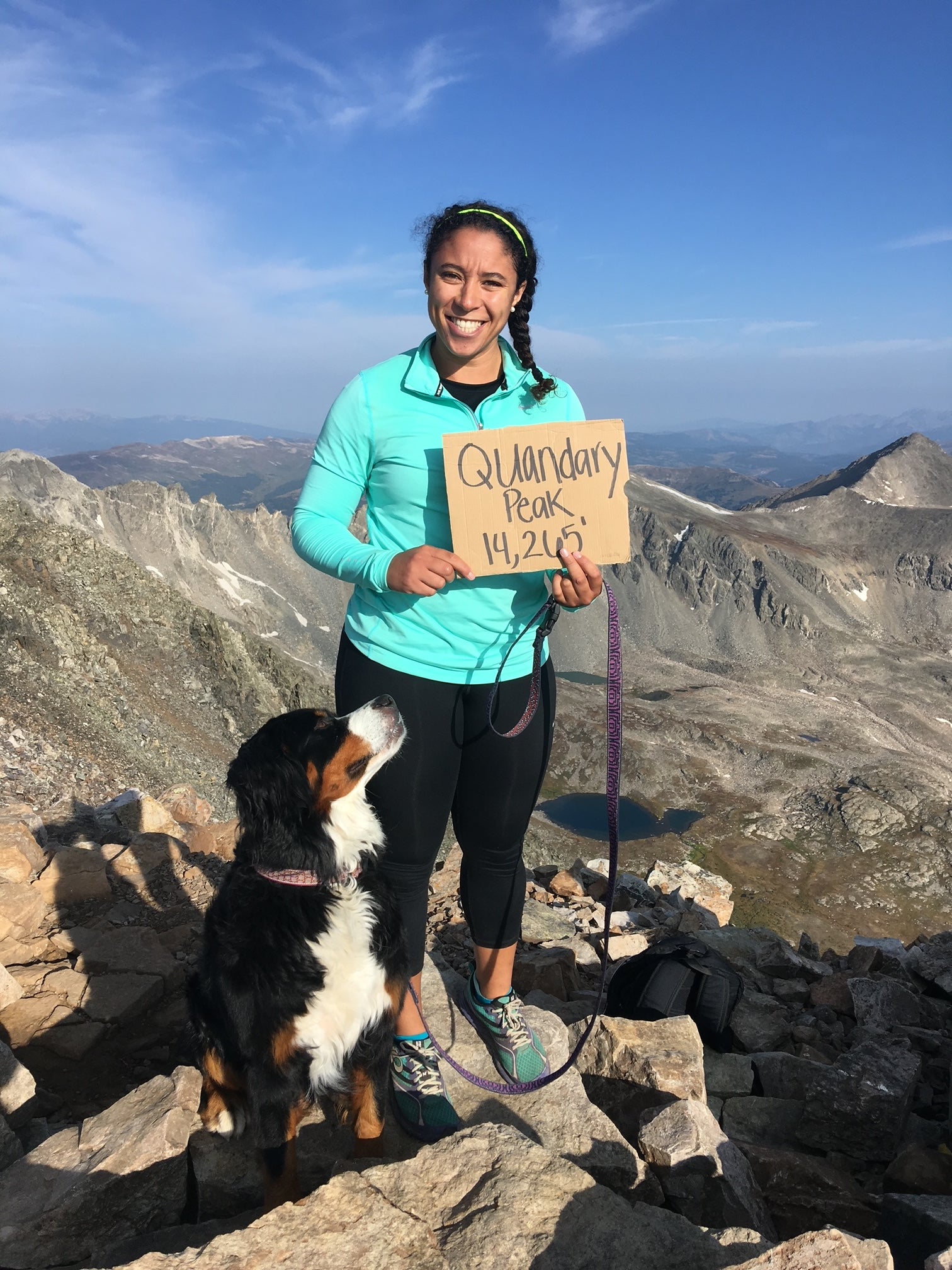 A woman stands with her Bernese Mountain Dog on top of Mount Sherman. 