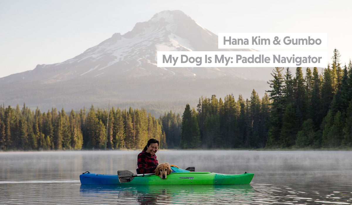 Hana paddles kayak on alpine lake with Gumbo in float coat in her lap