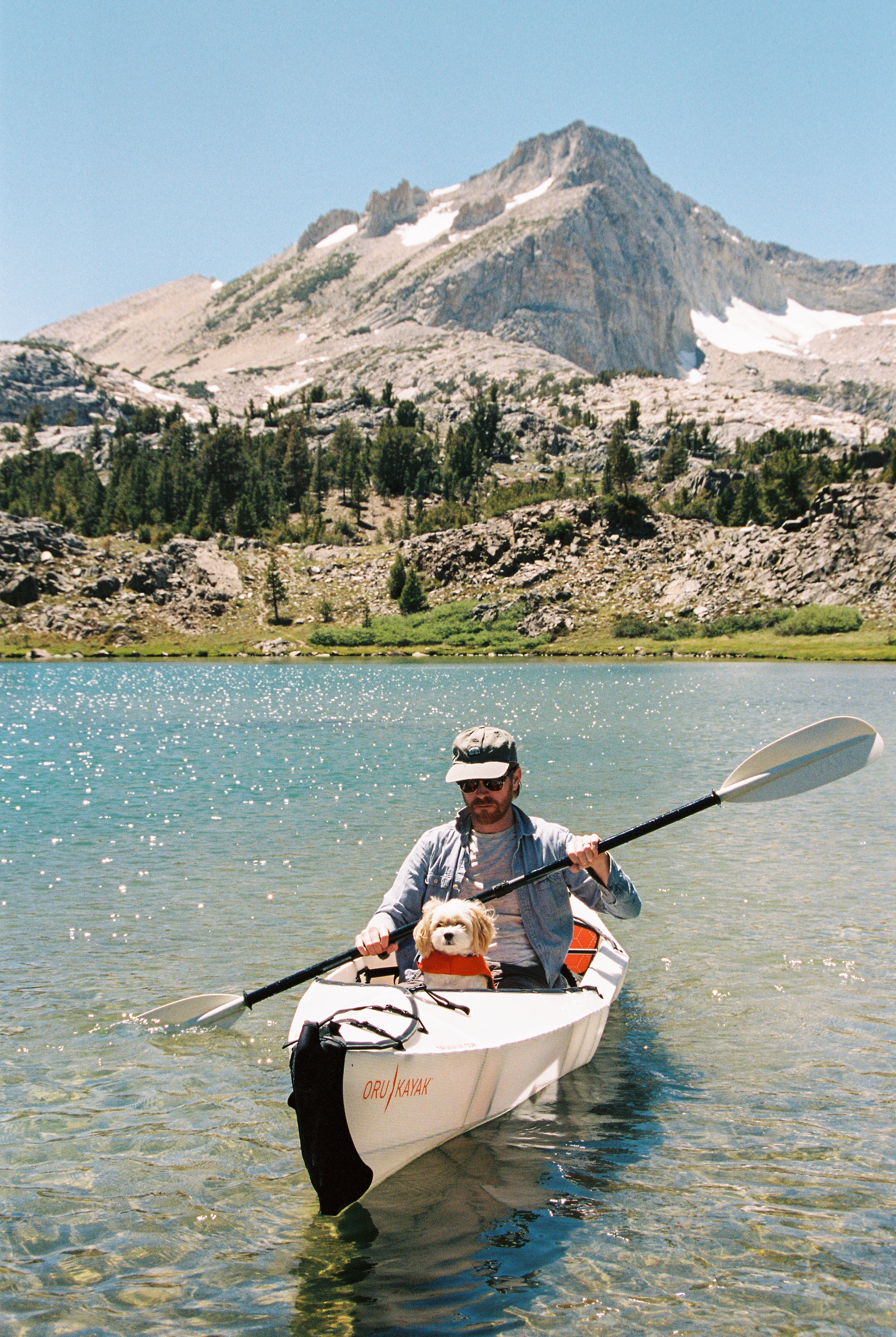 Small dog in a kayak with a guy on a lake with a mountain in the background