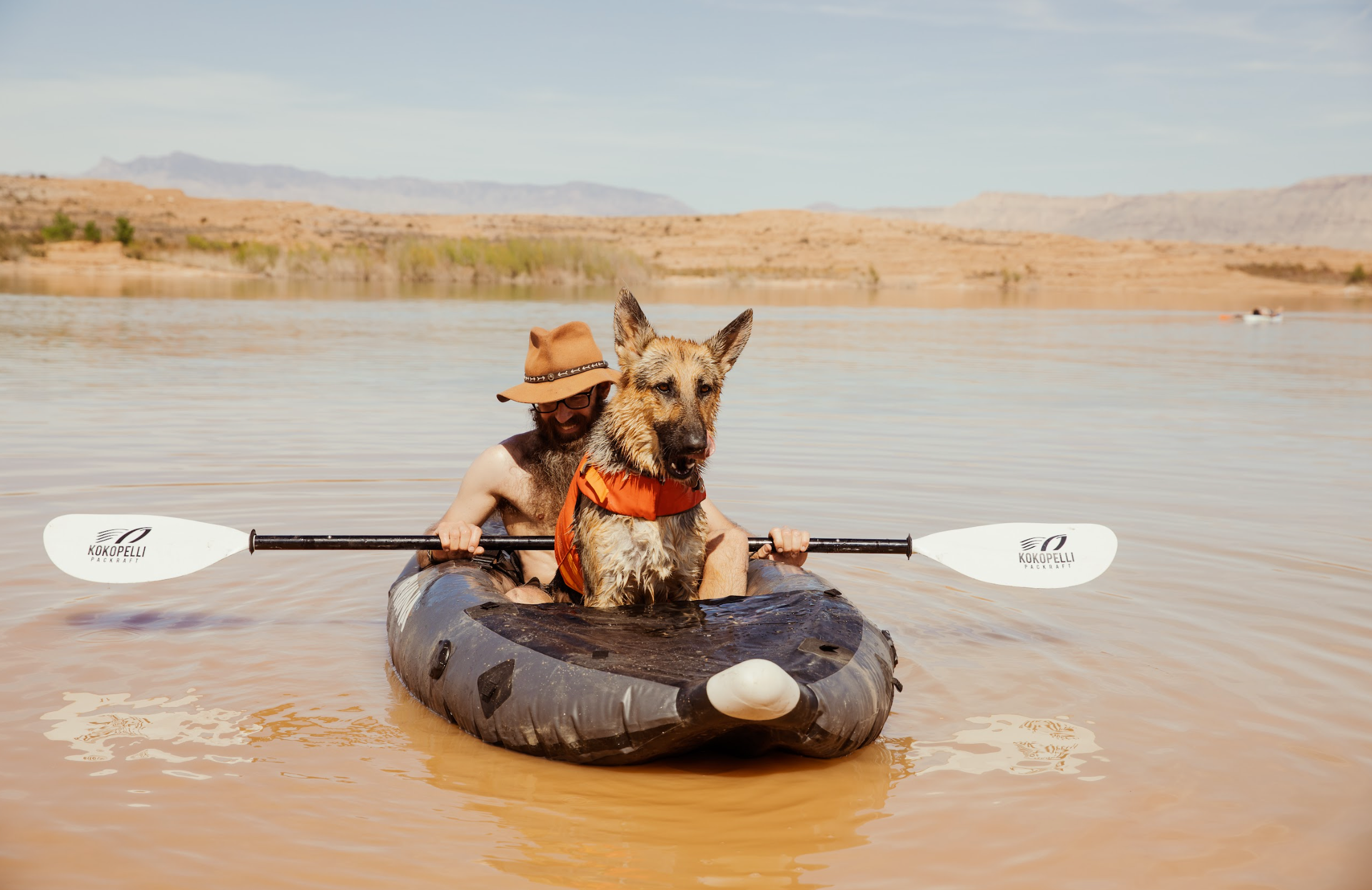 Man and dog in inflatable kayak paddling.