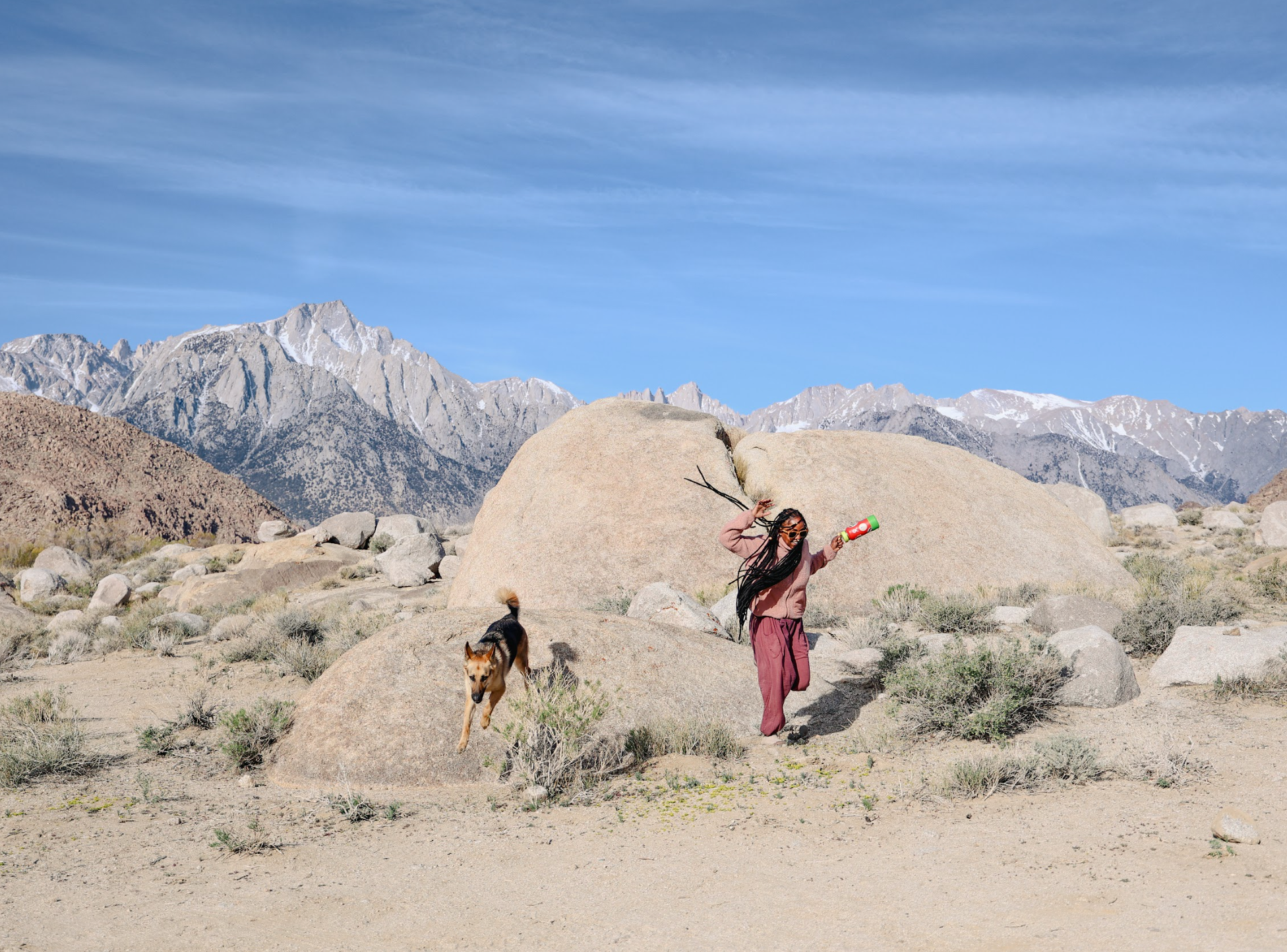 Woman and dog jump and play in a rocky desert.
