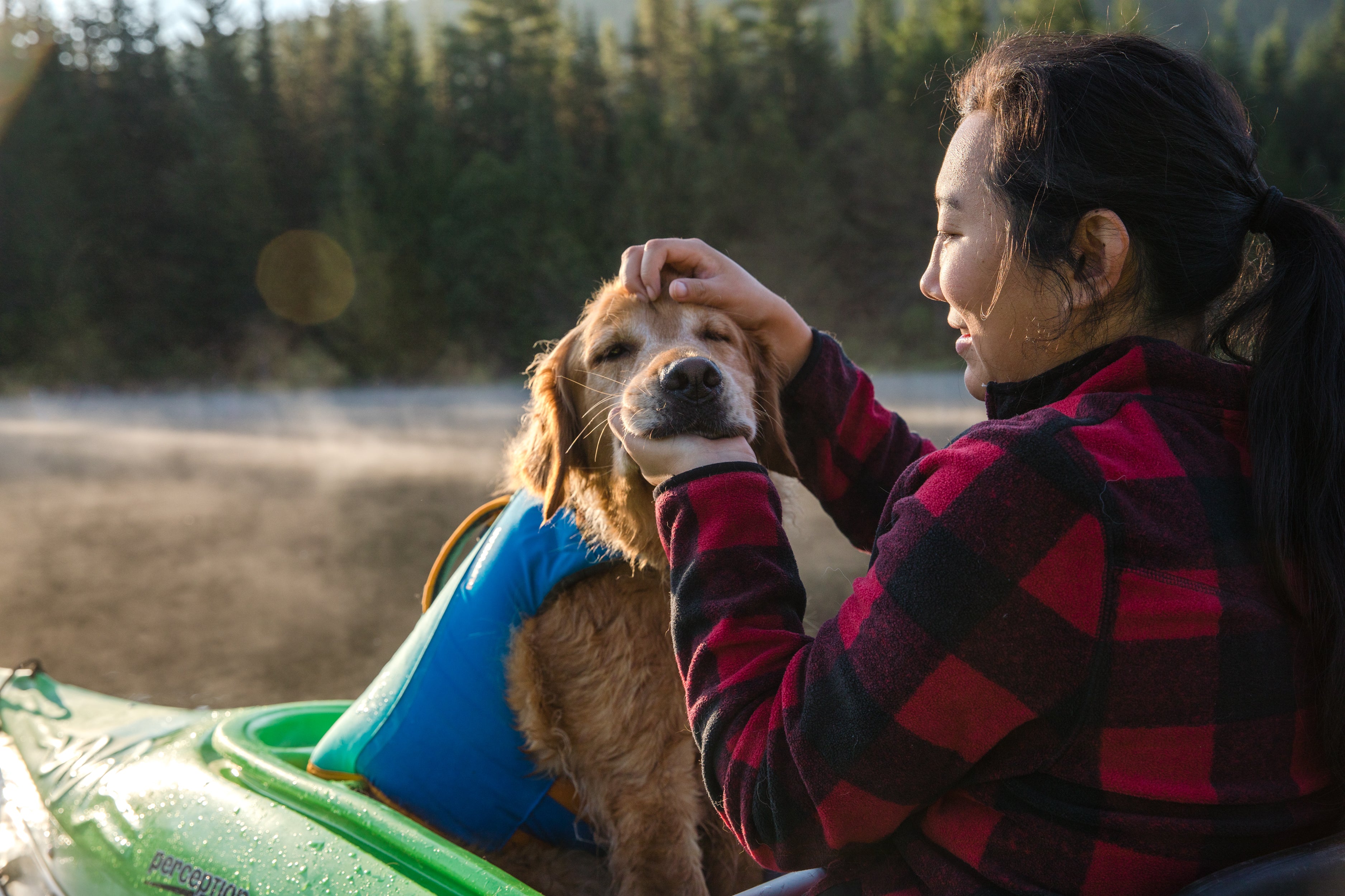 A woman pets her golden retriever who is sitting with her in a kayak. 