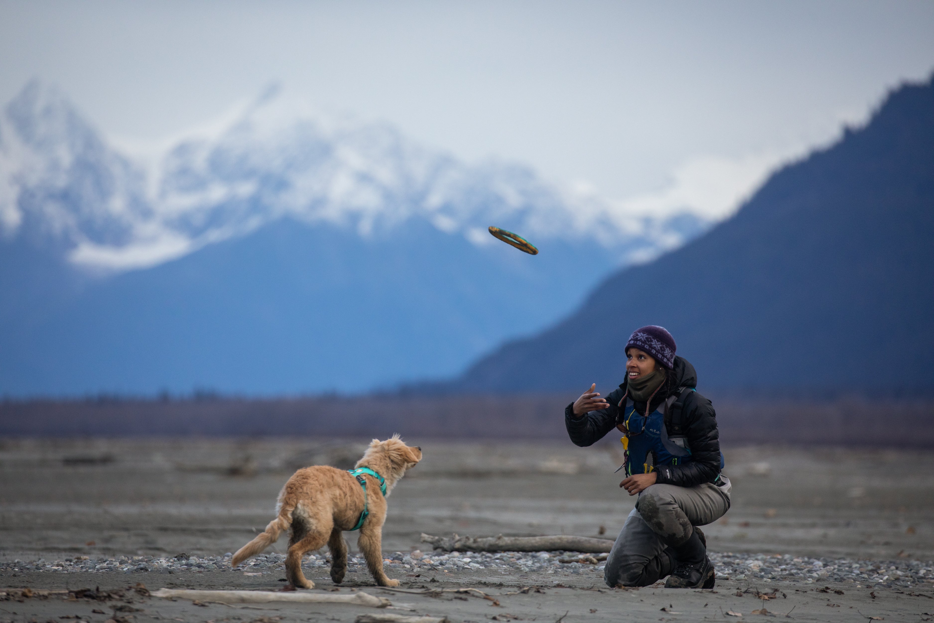 In the mountains, a woman throws a Hydro Plane™ toy in the air for her golden retriever puppy. 