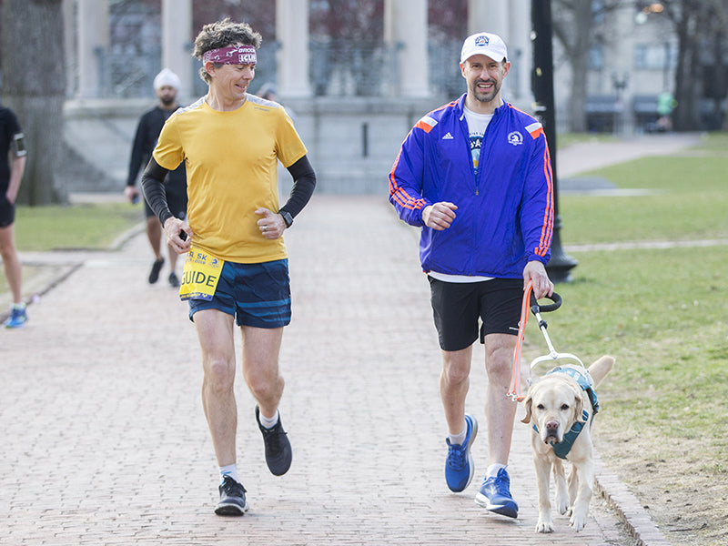 Blind runner in running race with human and dog guide at his side.