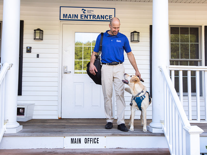 Human and dog in Unifly harness stand on porch of guiding eyes for the blind.