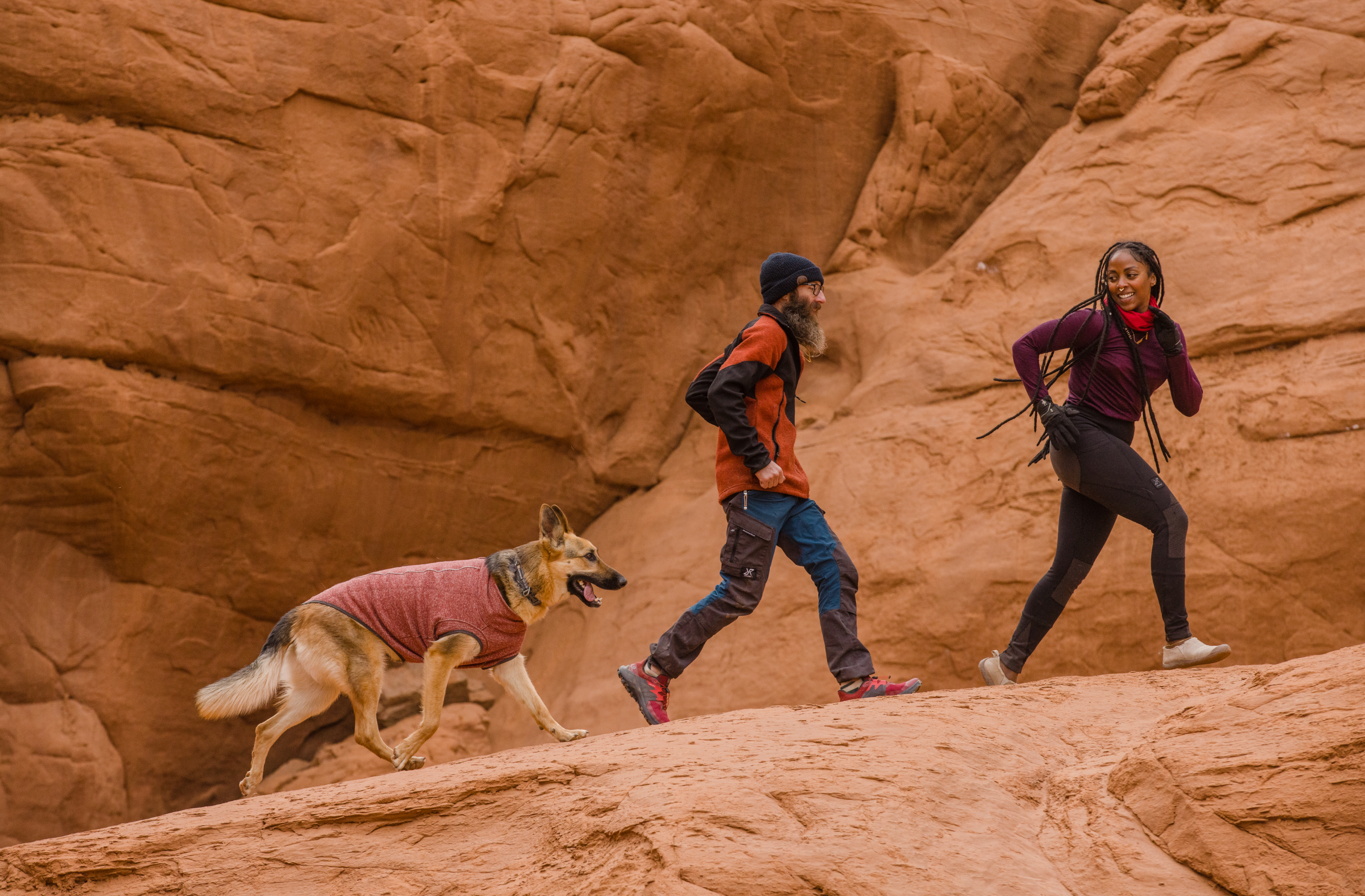 Woman and man running with dog in a desert canyon