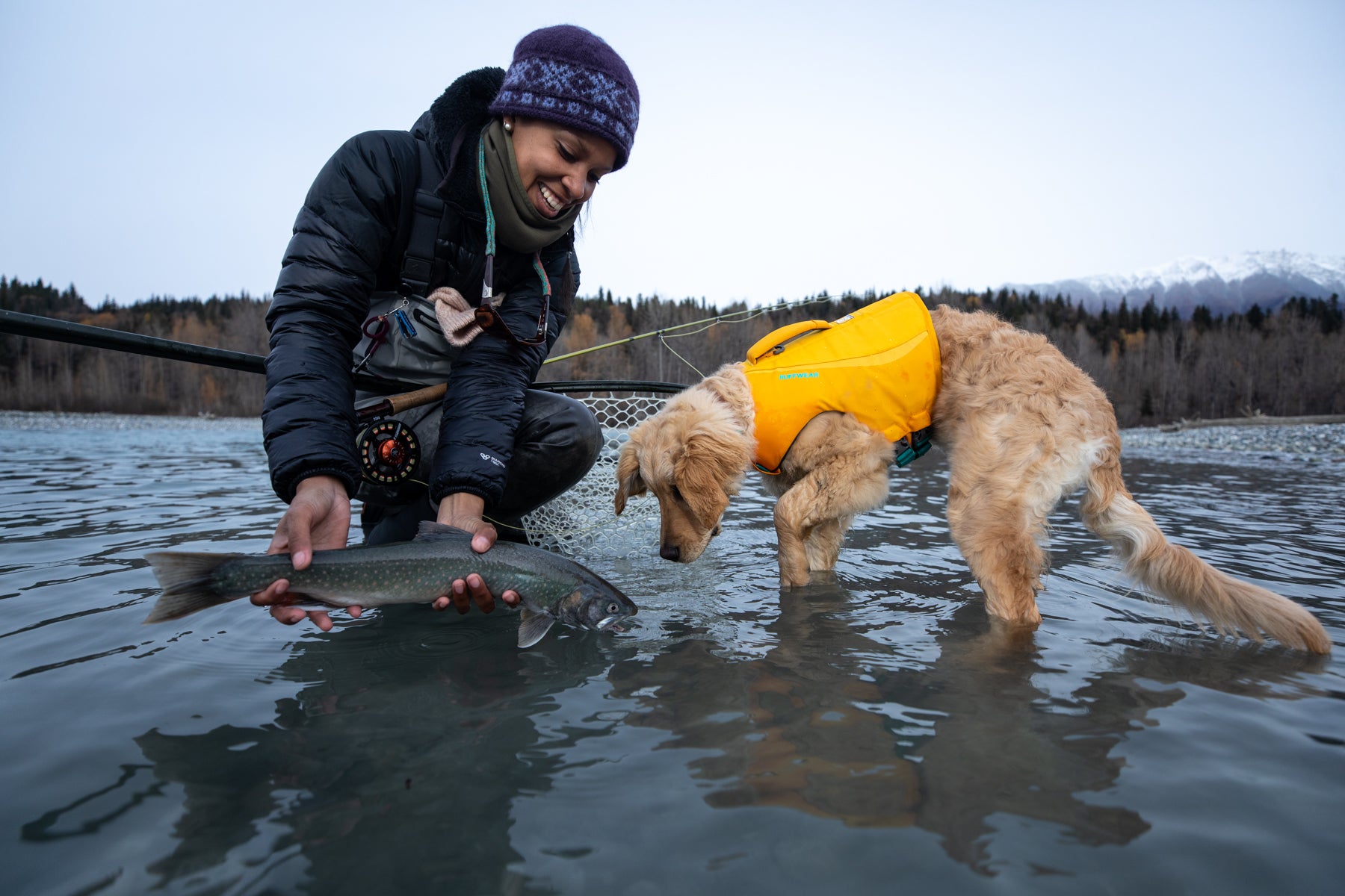 Chris holds fish while Sammy the puppy in float coat life jacket investigates.