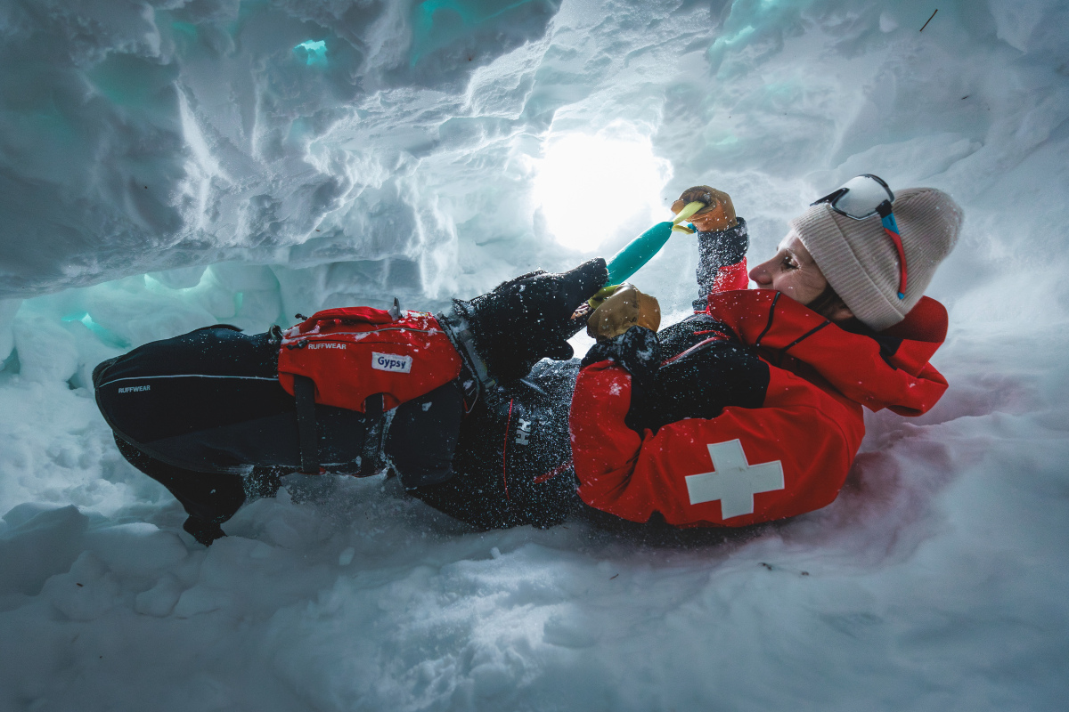 A Ruffwear employee and an avy dog playing in a snow cave.