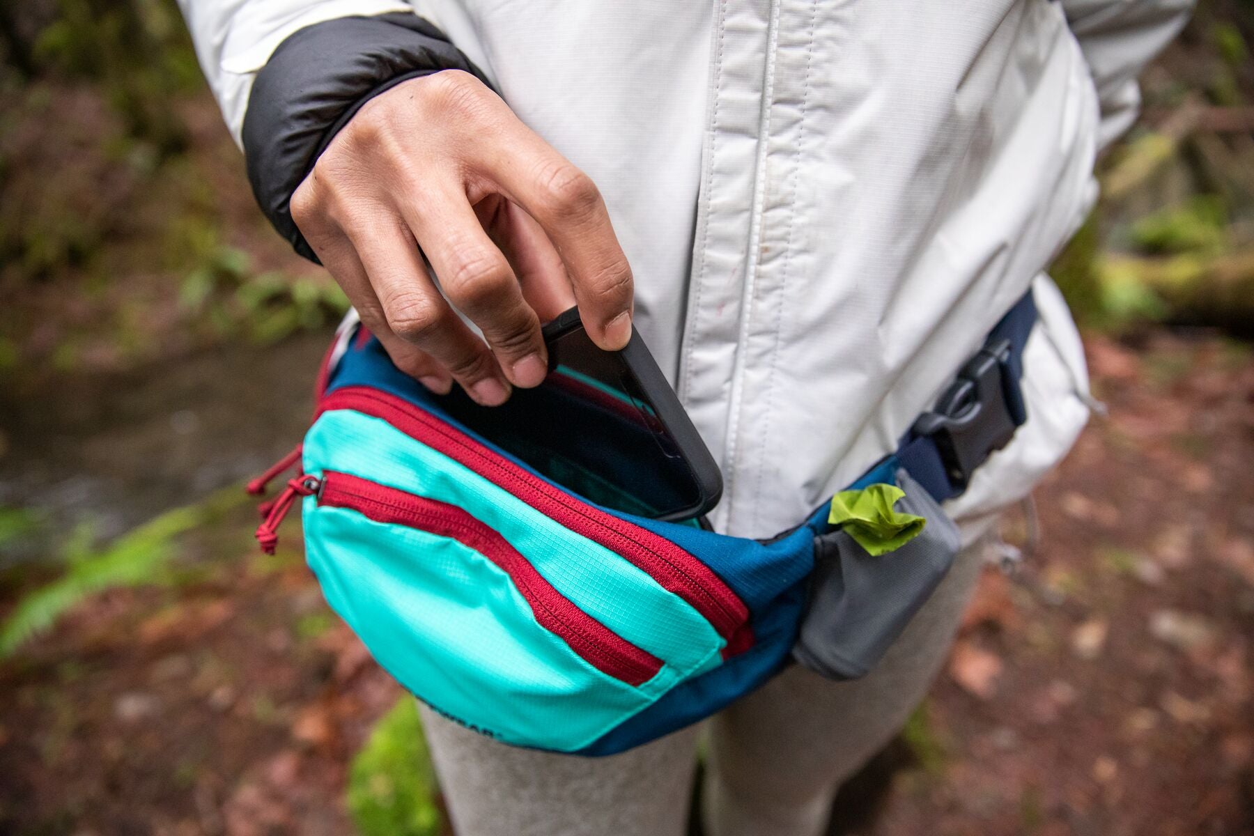 Human puts into phone pouch into home trail hip pack.