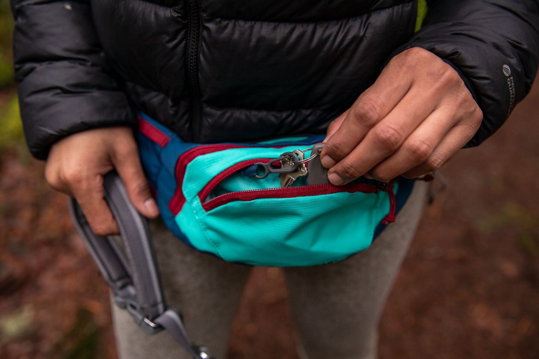 A woman wears the Ruffwear Home Trail™ Hip Pack around her waist and puts her keys in it.