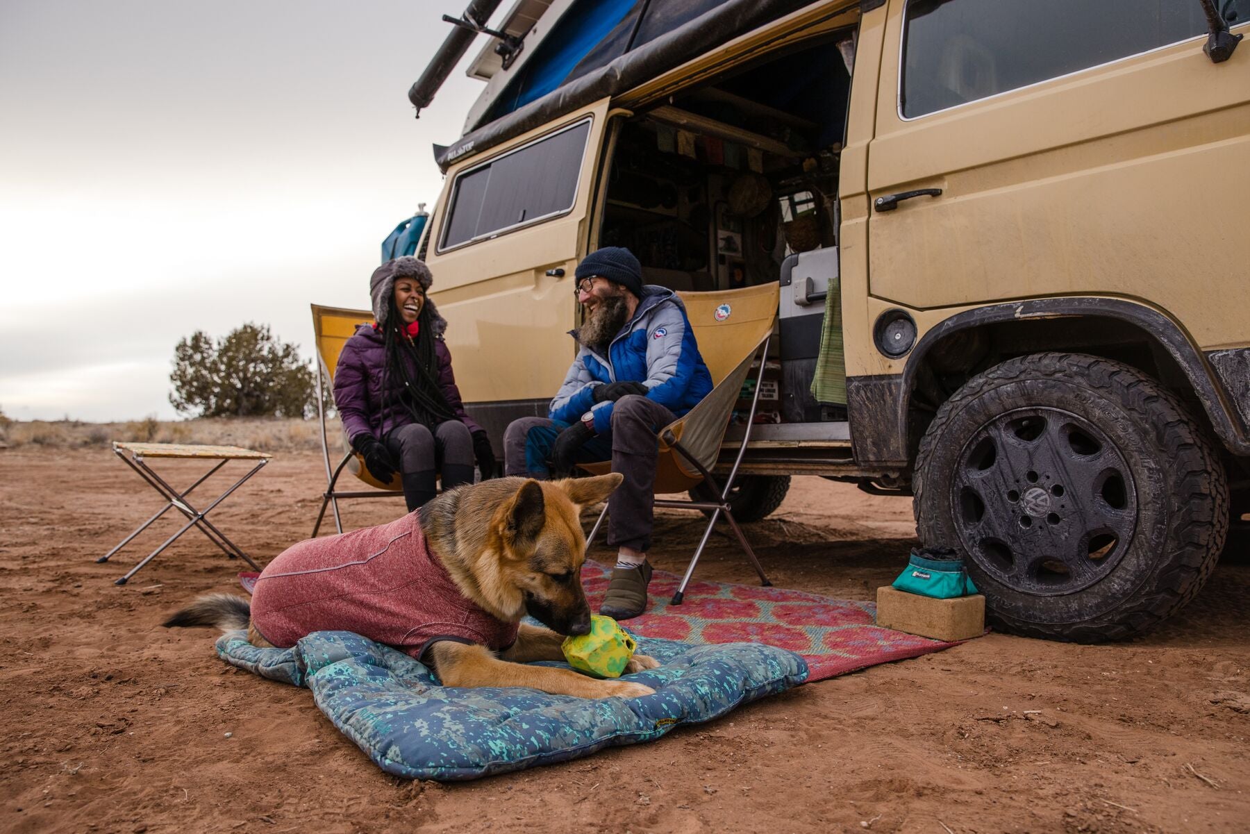 Dog and two humans sitting outside by their camper van