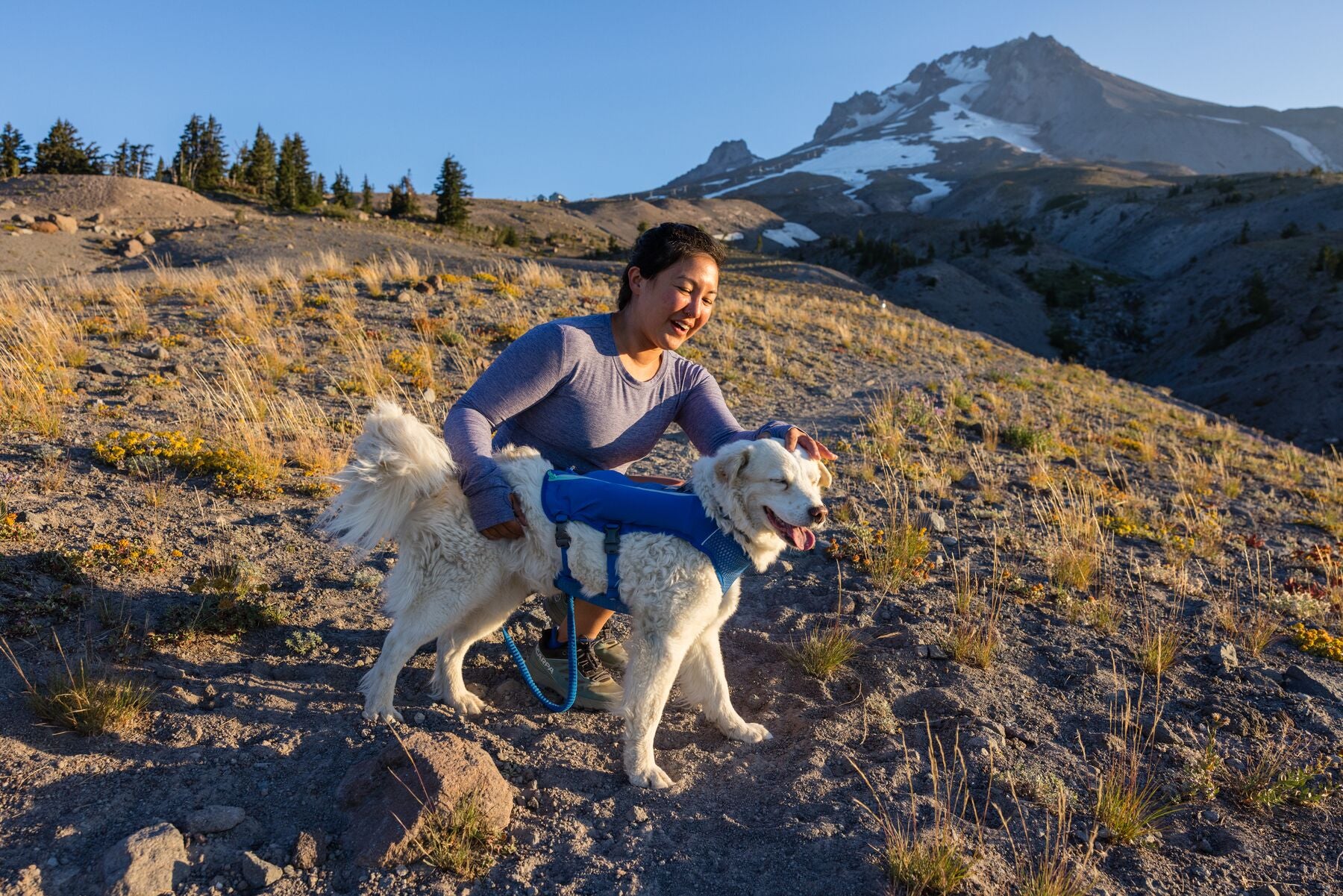 Woman crouching next to her dog on a trail