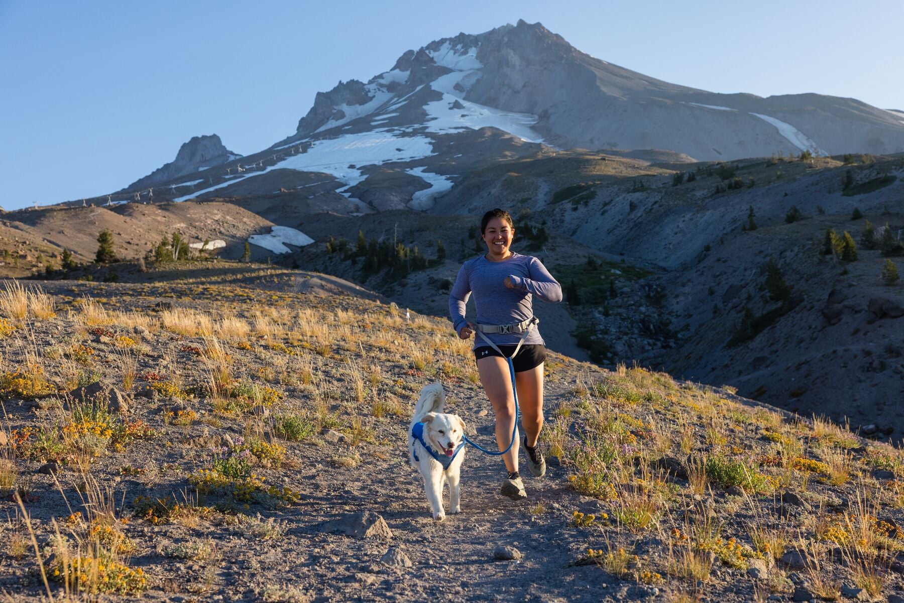 Woman and dog trail running together with a mountain in the background