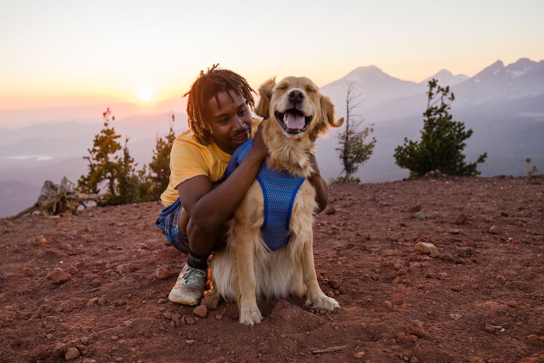 Man petting his dog and sitting together on a mounttop