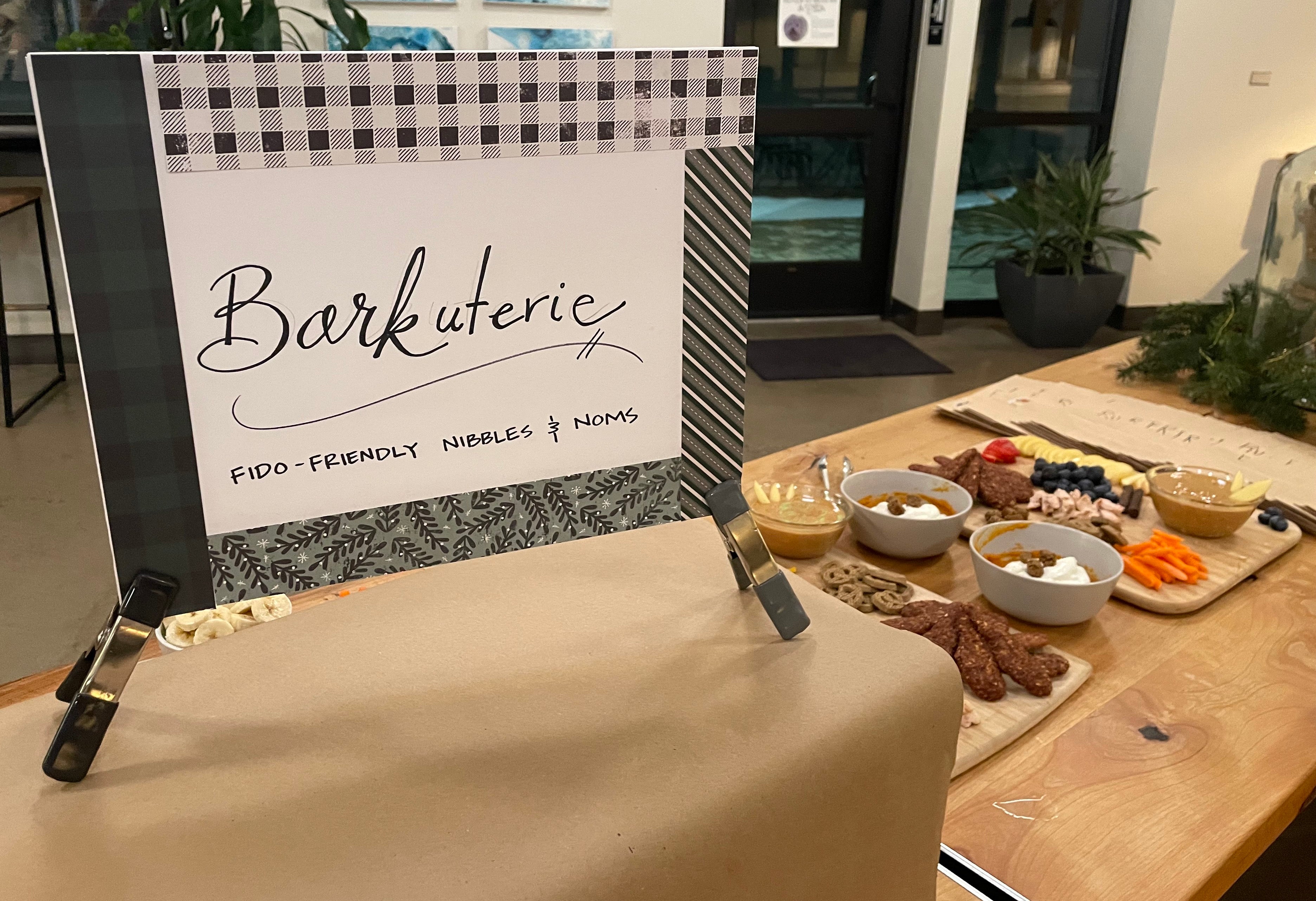 A sign saying "Barkuterie Board" and a platter of dog-friendly foods on a table.