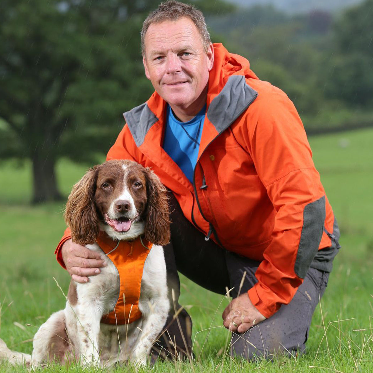 Kerry poses on the trail with his dog in an orange front harness that matches his raincoat.