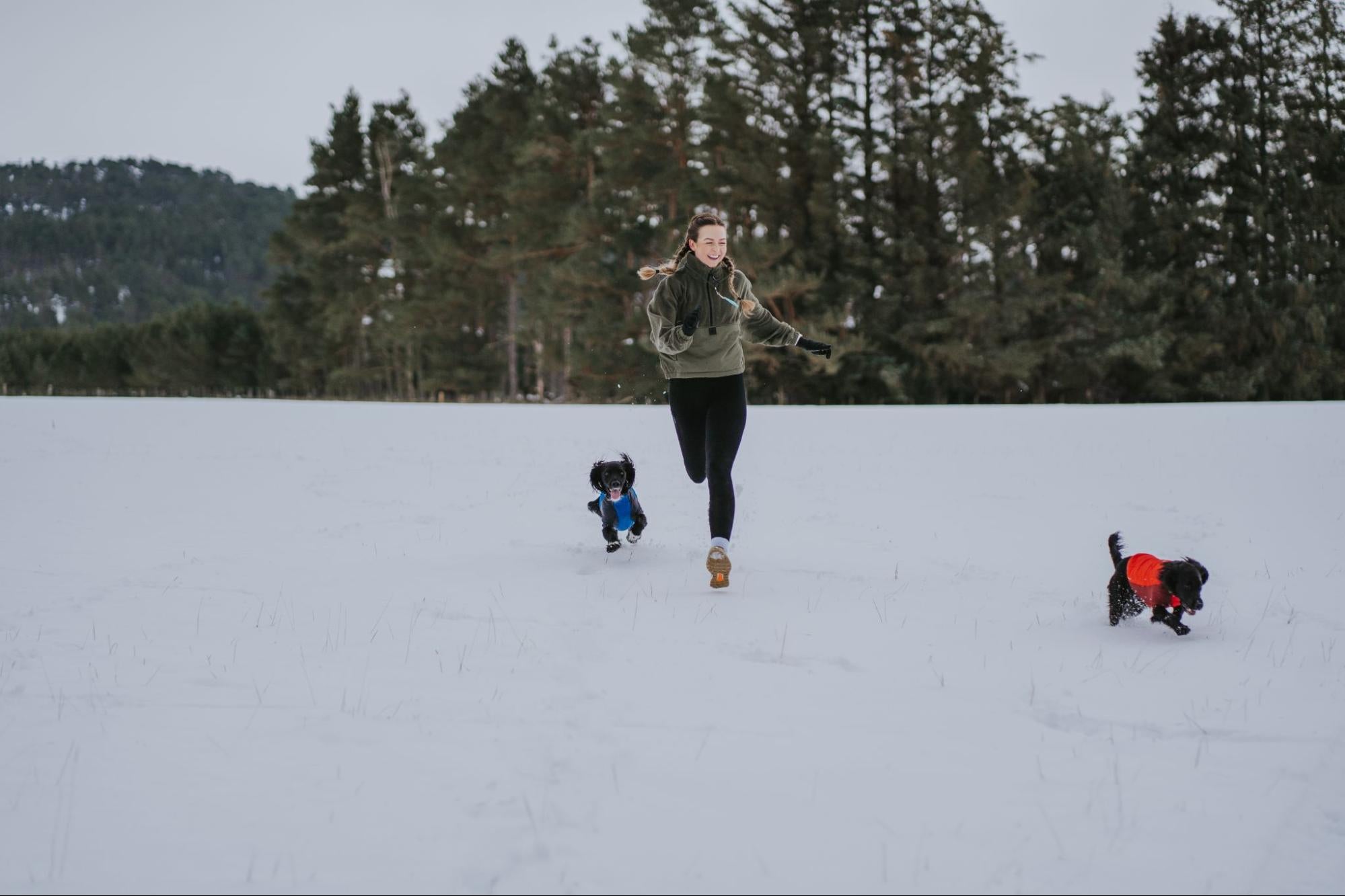 Woman running on the snow with two dogs