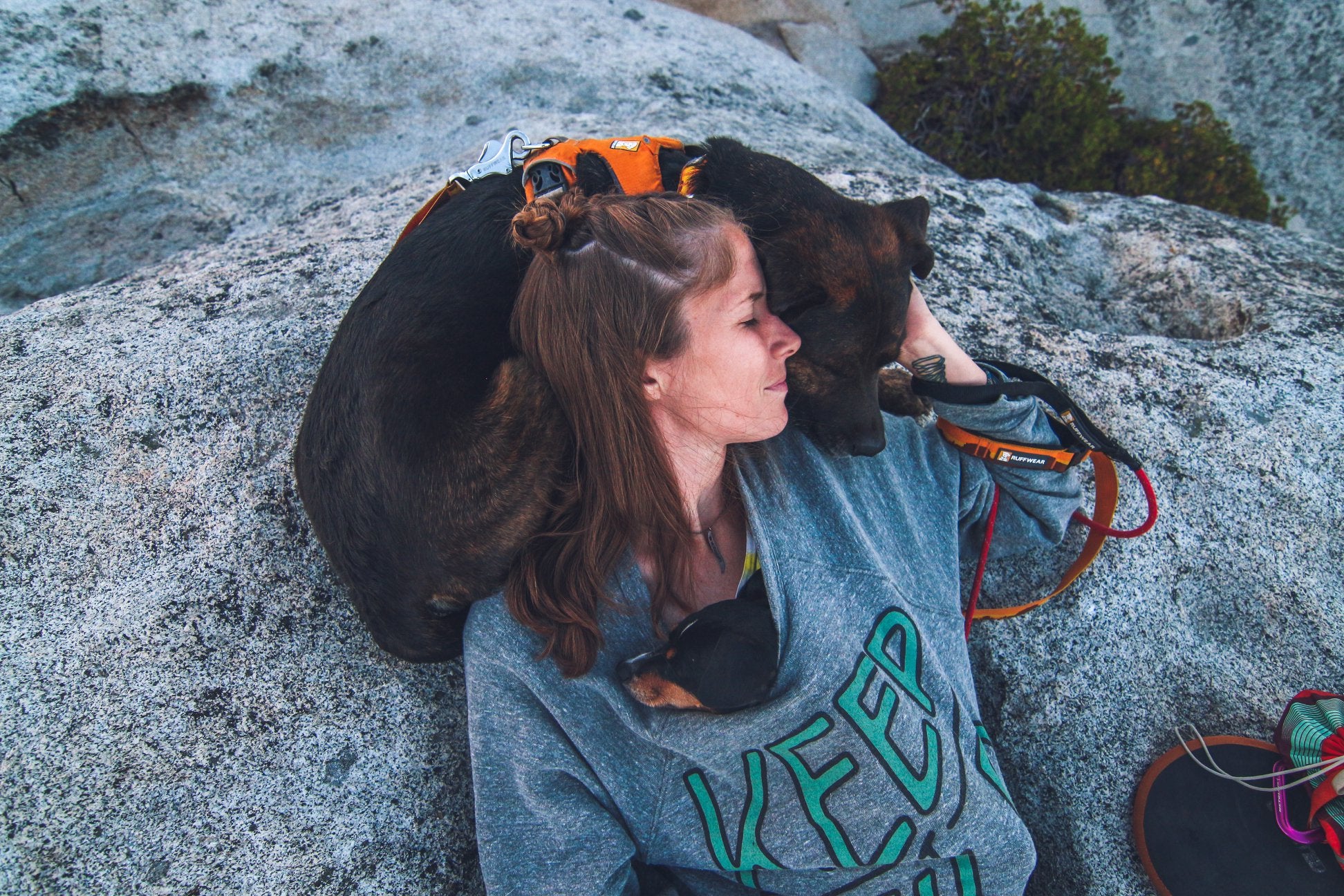 Woman snuggling with dog while sitting on a rock
