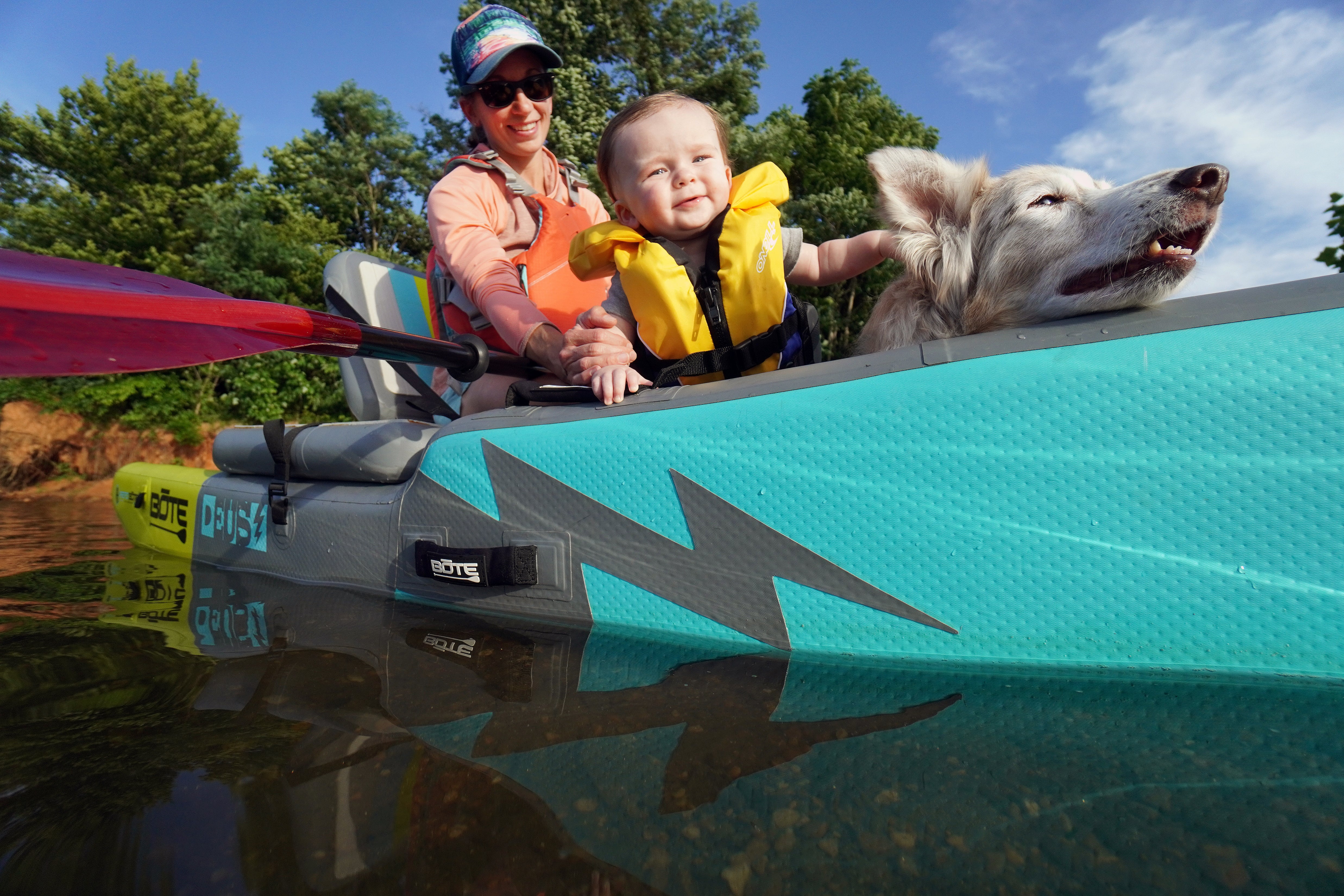 A woman sits in an inflatable kayak with her baby and dogs. 