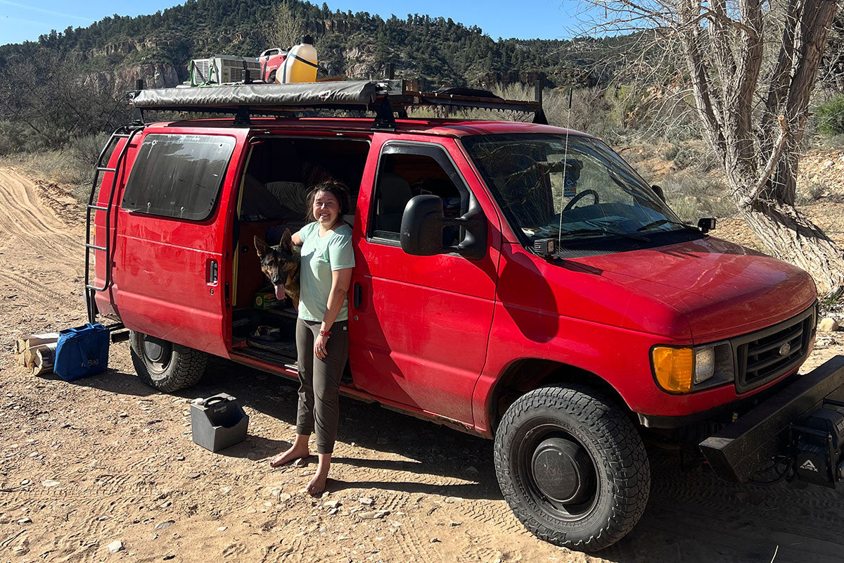 Zander sits in the doorway of Emma's red van on a dust road.