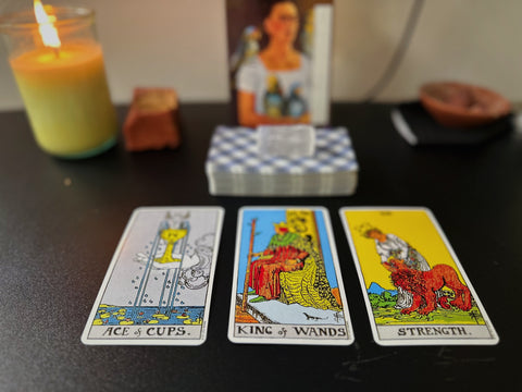 Three tarot cards on a black surface with a candle in the background
