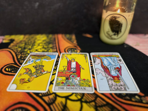 Three tarot cards on a tapestry with a candle in the background