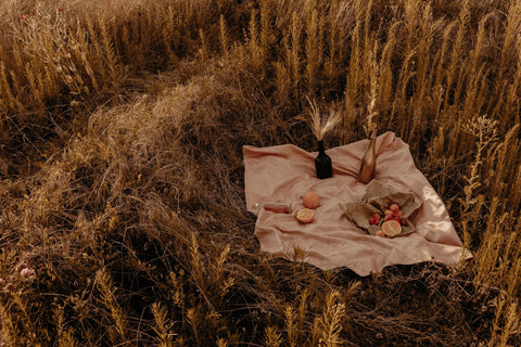 Bottles and baskets laid upon a blanket in a wheat field.