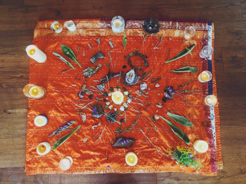 Orange blanket with candles, leaves, flowers, and other pieces of nature gathered in a mandala