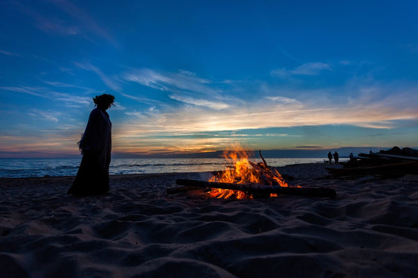 silhouette of someone in a flower crown on a beach by a fire as the sun rises or sets