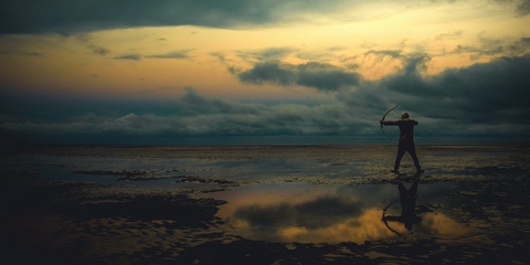 A silhouetted figure stands poised to shoot an arrow from their bow, against a sunset in a watery landscape