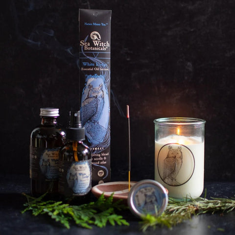 Sea Witch Botanicals White Lodge gift set with incense, spray, solid perfume, and candle, pictured with fresh boughs of cedar and fir, incense and candle burning.