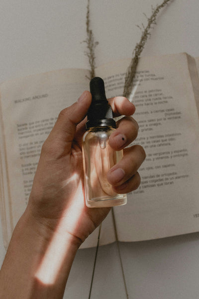 Person holding a small clear dropper bottle with an open book in the background.