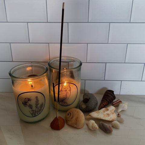 Two candles and incense sticks burning on a white background with an assortment of shells and stones