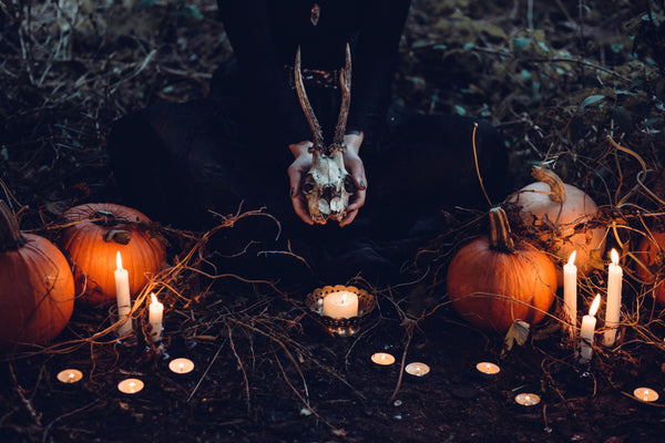 pumpkins and burning candles and a person holding a horned skull, darkly lit