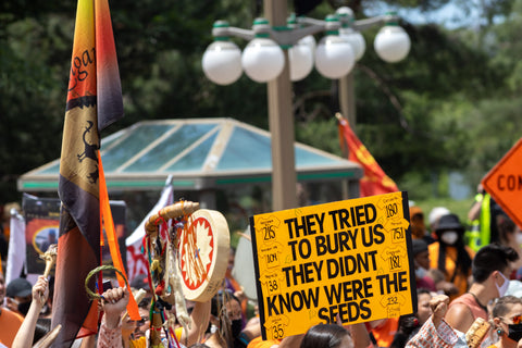 A sign held up at a Canada Day protest against treatment of Indigenous people in Canada reads: "They tried to bury us / They didn't know were the seeds"