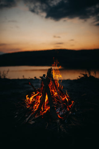 Bonfire burning low by a lake at dusk