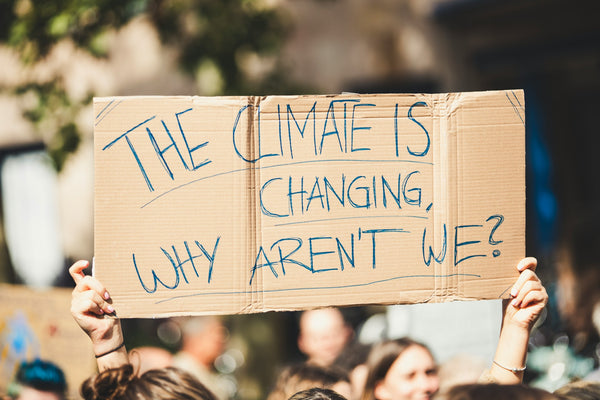 A group of people holding a sign that says "The climate is changing why aren't we?"