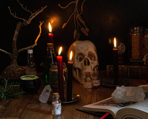 gathering of burning candles, crystals, skull, and an open book on a wooden table.