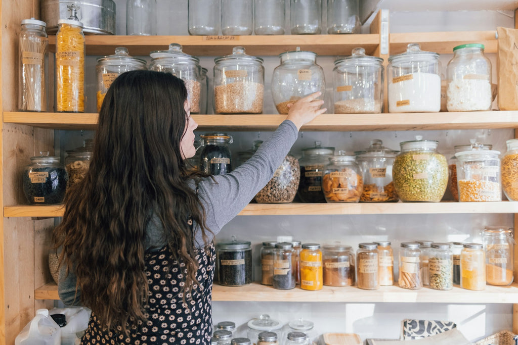 A person holding a jar of food along a shelf of other glass jars.