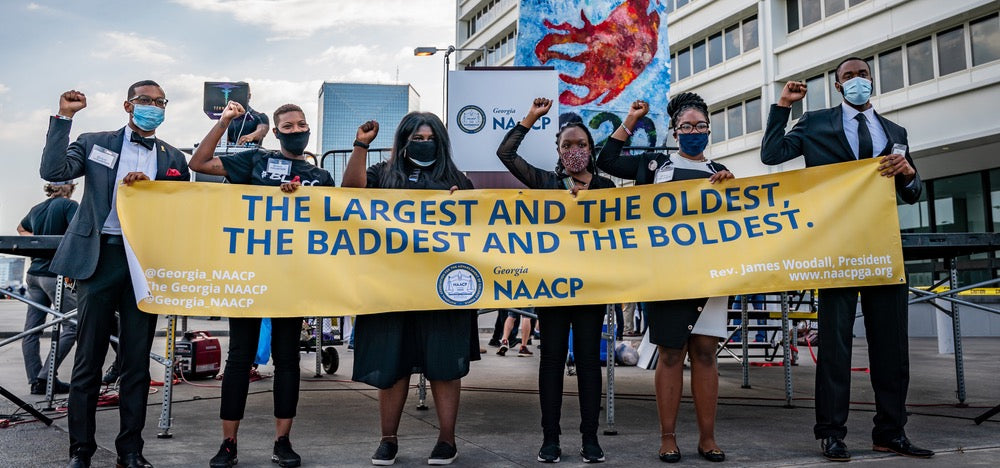 Scene from the NAACP-sponsored rally and march to the Georgia State Capitol on June 15, 2020, which focused on voting rights, police brutality, and criminal legal reform. Group of Black folks wearing masks holding an NAACP banner that reads: "THE LARGEST AND THE OLDEST, THE BADDEST AND THE BOLDEST"