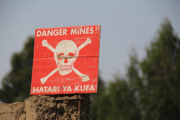 White skull-and-crossbones symbol on a red sign warning of the danger of landmines, Democratic Republic of Congo