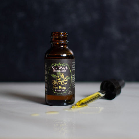 Opened bottle of Fae Ring Scented Oil with dropper on marble countertop, dark background.