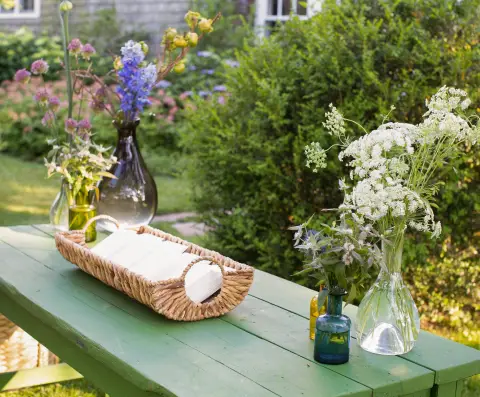 A table with floral arrangements in vases and napkins is in an outdoor setting.