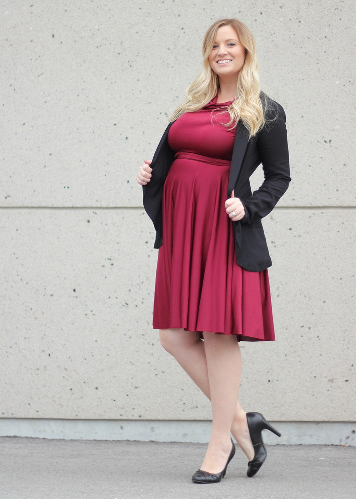 5 Mothers Day outfit ideas: blonde pregnant woman wearing a Henkaa convertible dress in dark pink and a dark grey coat on top.