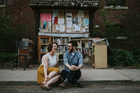 Averie MacDonald and Bled Celhyka pose for engagement photos in front of a bookstore.
