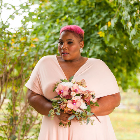 Women in Henkaa Apricot Coral Infinity dress holding bouquet of flowers at Country Heritage Park.