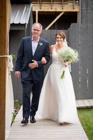 Ashley's father walks her down the aisle, Ashley holds a large bouquet of Baby's-breath. 