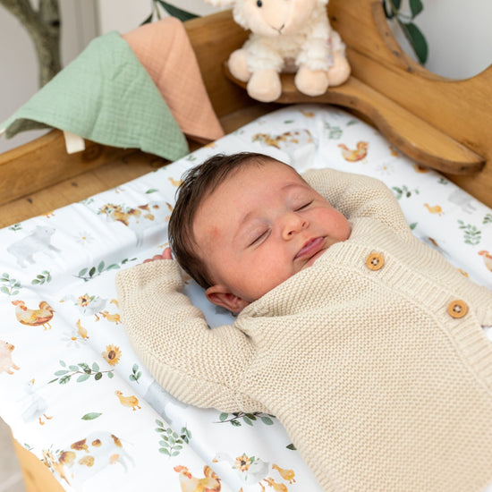 Baby lying on  a Mabel & Fox farmyard animals print changing mat.