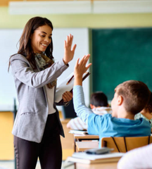 Happy elementary school teacher giving high-five to her student during class in the classroom. stock photo