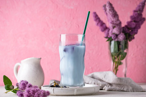 blue purple lavender banana milk with purple flowers and small milk pitcher on purple background